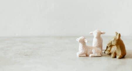 Two white sheep figurines and one brown animal figurine on a light gray surface with a light gray background