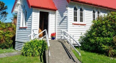 Gray ramp up to the entrance of a white building with a red roof