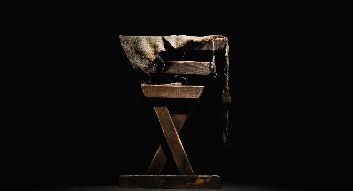 Wooden manger with burlap cloth draped over its side in front of a black background