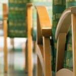 Close-up of several chairs arranged in rows back-to-back with wooden arms and legs and multi-colored green and blue cushions