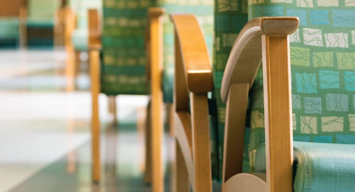 Close-up of several chairs arranged in rows back-to-back with wooden arms and legs and multi-colored green and blue cushions