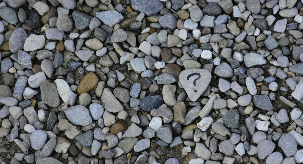 A gray, triangle-shaped rock with a dark question mark on it surrounded by numerous small rocks in various colors