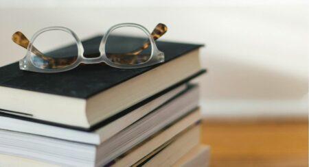 Close-up of a pair of glasses on top of a stack of books with an ivory and light brown background