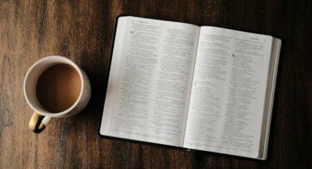 Aerial view of a mug containing brown liquid beside a Bible open to Isaiah in front of a brown wooden background