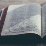 Close-up of open Bible on a wooden surface with sunlight and shadows scattered across the pages and surface