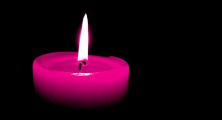 Close-up of the top of a lit pink candle surrounded by a black background