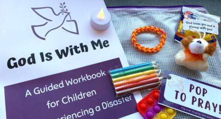 "God Is With Me" workbook with a series of accompanying objects: (from top middle clockwise) a battery-powered tealight candle, a red, orange, and yellow bracelet, a snack package, a stuffed animal, a popsocket keychain with a card "Pop to Pray!" and a package of 6 colored pencils