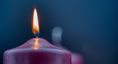 Close-up of lit purple candle in front of a blurred unlit purple candle and a dark blue background