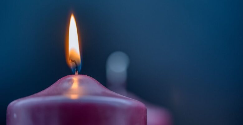 Close-up of lit purple candle in front of a blurred unlit purple candle and a dark blue background