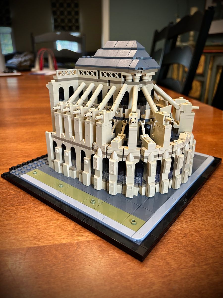 Angled side view of flying buttresses of Lego Notre Dame Cathedral on a tan wood surface with black chairs and teal walls in the background