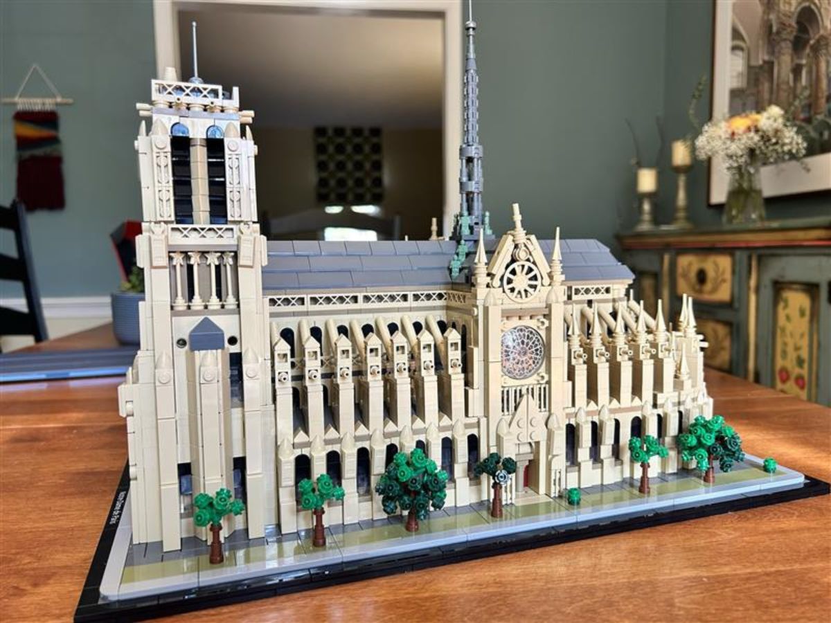 Angled side view of fully constructed Lego Notre Dame Cathedral on a tan wood surface with teal walls and other furnishings and decorations in the background