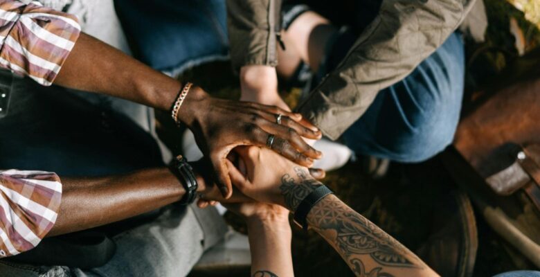 Close-up of multiple human hands with dark, medium light, and light skin tones stacked together