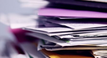 Close-up of disheveled stack of mail with envelopes in various colors, like light purple, white, brown, and yellow