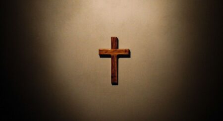 Wooden dark brown cross on a light brown surface in a spotlight
