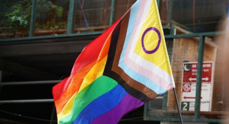 Pride flag on a black pole outdoors in front of a window