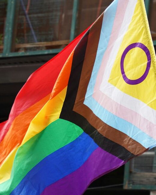 Pride flag on a black pole outdoors in front of a window