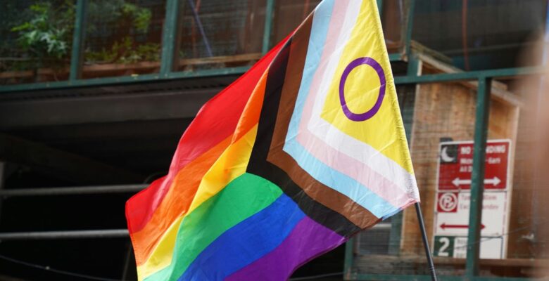 Pride flag on a black pole outdoors in front of a window
