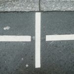 Two white arrows pointing outward in opposite directions with a vertical white line between them on dark gray pavement