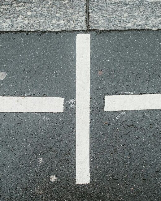 Two white arrows pointing outward in opposite directions with a vertical white line between them on dark gray pavement
