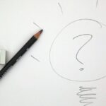 Gray pencil drawing of question mark in a circle surrounded by short rays along the top and a spiral squiggle at the bottom with a white eraser and gray pencil to the left on an off-white background