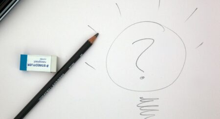Gray pencil drawing of question mark in a circle surrounded by short rays along the top and a spiral squiggle at the bottom with a white eraser and gray pencil to the left on an off-white background