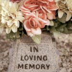 Close-up of light gray and black speckled stone with text that says "IN LOVING MEMORY" and a bouquet of ivory, peach, and pink flowers perched on top