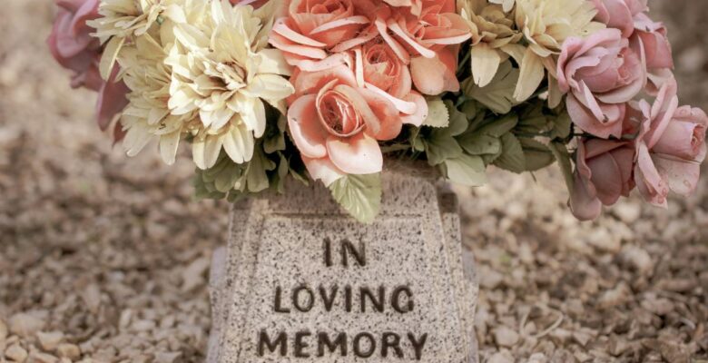 Close-up of light gray and black speckled stone with text that says "IN LOVING MEMORY" and a bouquet of ivory, peach, and pink flowers perched on top