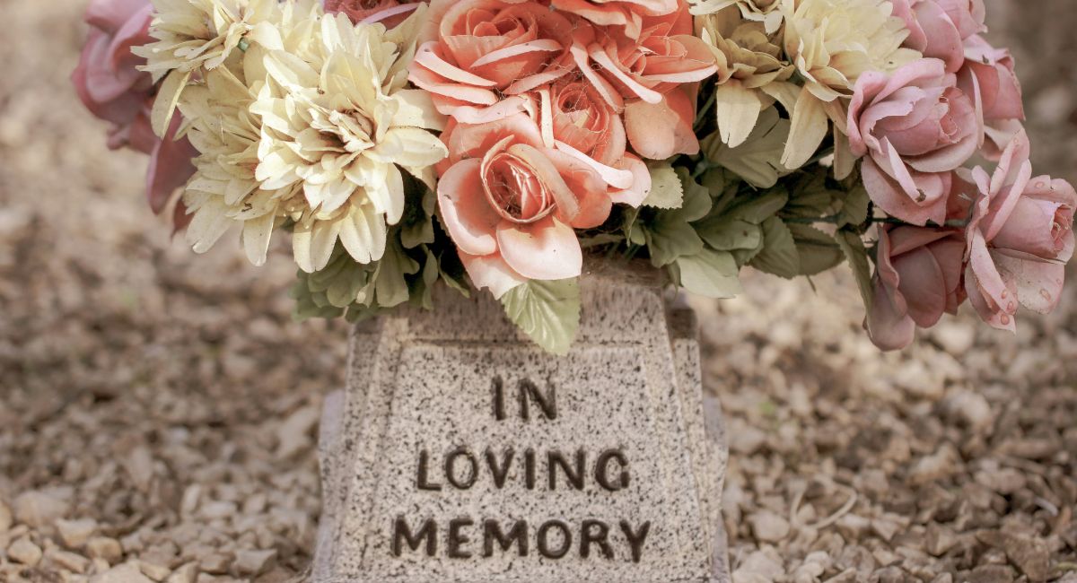 Close-up of light gray and black speckled stone with text that says "IN LOVING MEMORY" and a bouquet of ivory, peach, and pink flowers perched on top