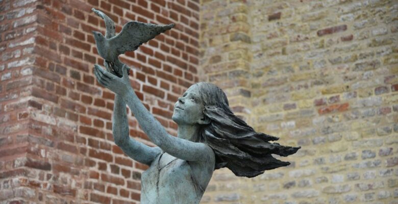 Close-up of a copper statue of a human figure that appears to be a woman with long hair releasing a bird with wings outstretched
