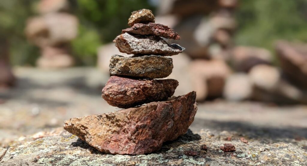 Six red, brown, and gray rocks stacked vertically on a rough rocky surface