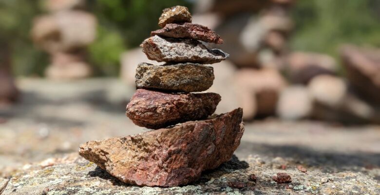 Six red, brown, and gray rocks stacked vertically on a rough rocky surface