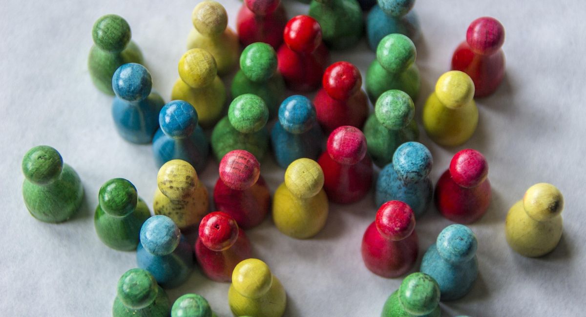 Aerial view of a bunch of board game figures in green, blue, yellow, and red on a gray surface