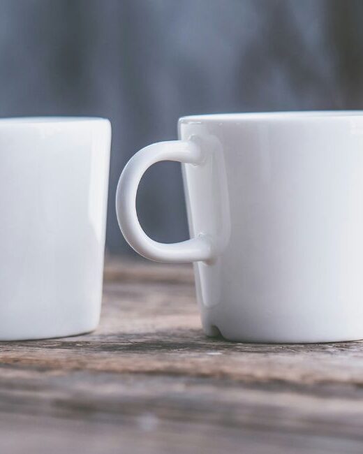 Two white ceramic mugs with handles on a brown wooden surface in front of a blue-gray background
