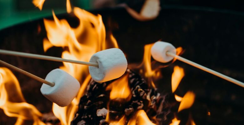 Three marshmallows on wooden sticks roasting over a fire