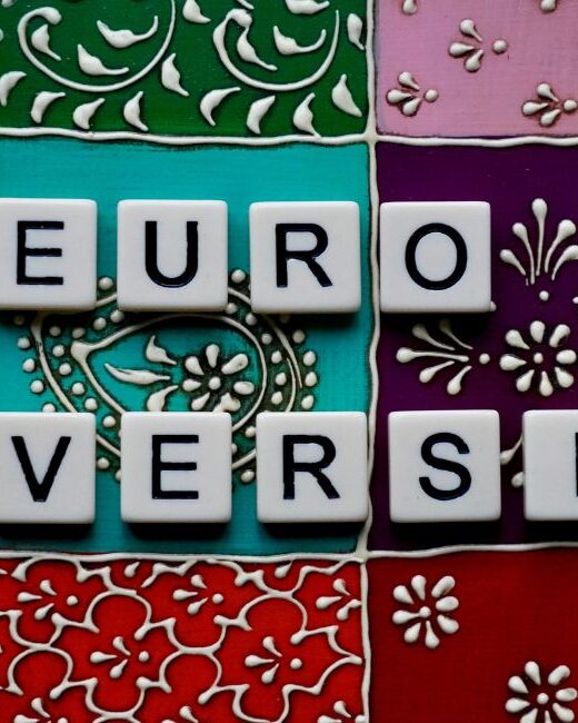 White tiles with black letters that say "NEURODIVERSITY" on a background of multi-colored blocks with various designs in black and white