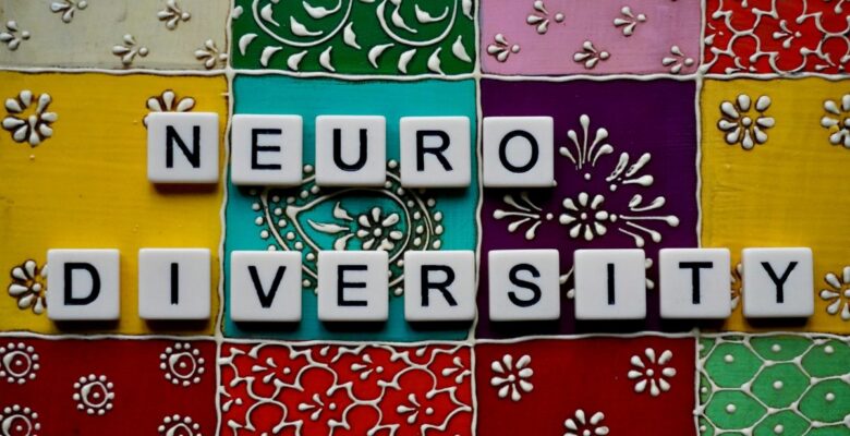 White tiles with black letters that say "NEURODIVERSITY" on a background of multi-colored blocks with various designs in black and white