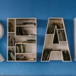 White shelving units in the shape of the letters "READ" holding numerous books and attached to a blue wall