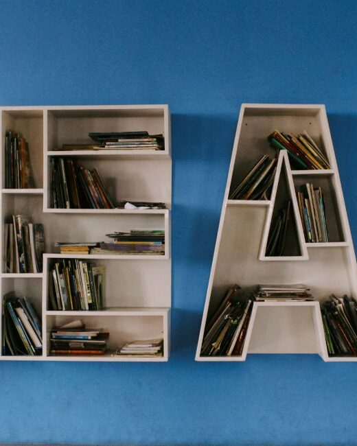 White shelving units in the shape of the letters "READ" holding numerous books and attached to a blue wall