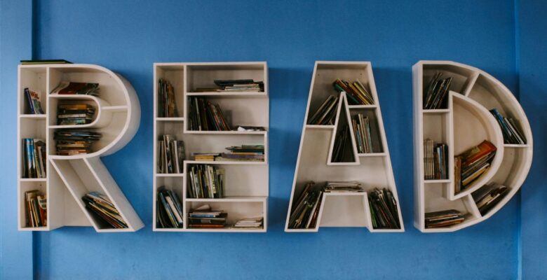 White shelving units in the shape of the letters "READ" holding numerous books and attached to a blue wall