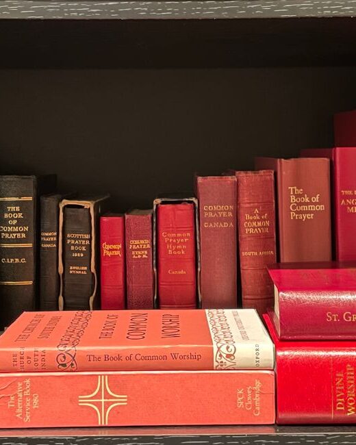 A collection of various editions of the Book of Common Prayer, derivatives, and associated liturgical texts on a dark brown bookshelf