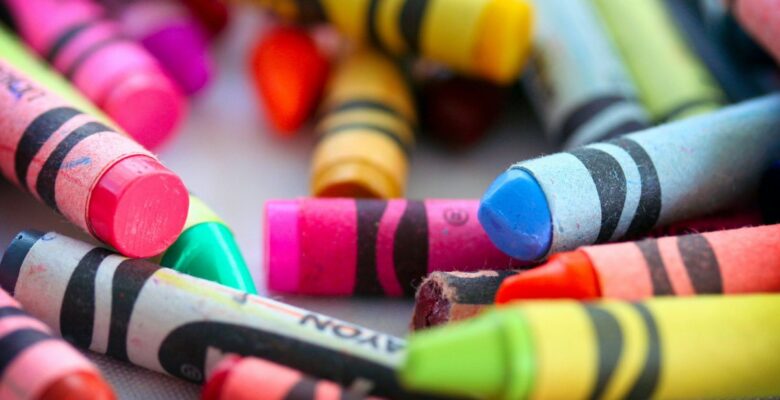 Close-up of many crayons in different colors in disarray on a gray surface