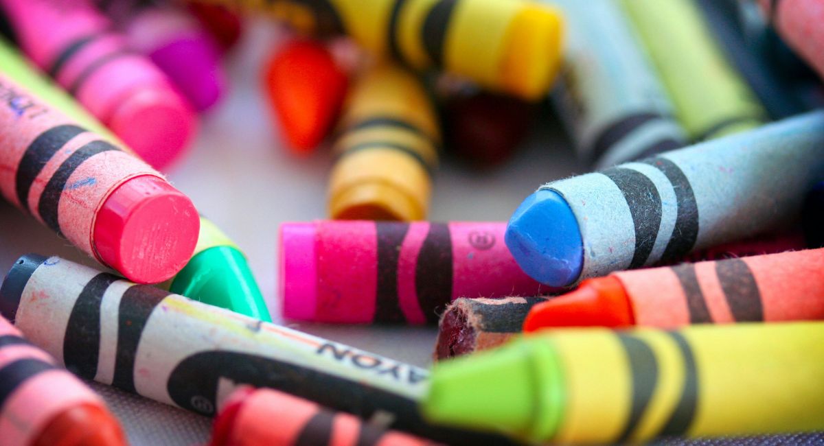 Close-up of many crayons in different colors in disarray on a gray surface